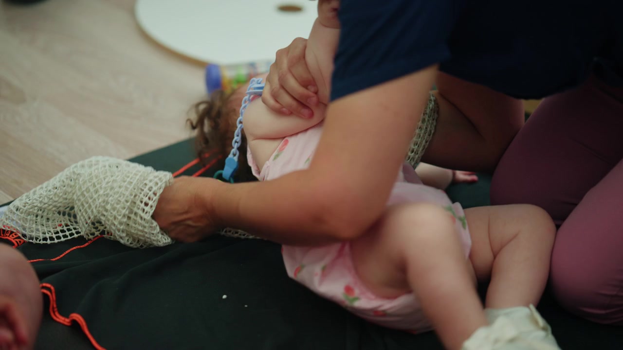 Neonato con un giocattolo sensoriale a rete durante una sessione di fisioterapia, promuovendo lo sviluppo attivo e le capacità motorie.