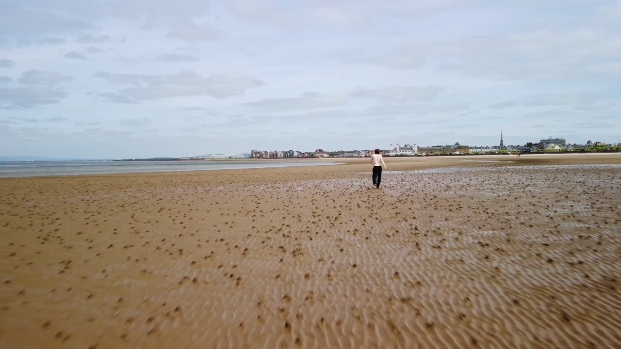 Aerial dolly footage of a young man on a beach near the water&rsquo;s edge