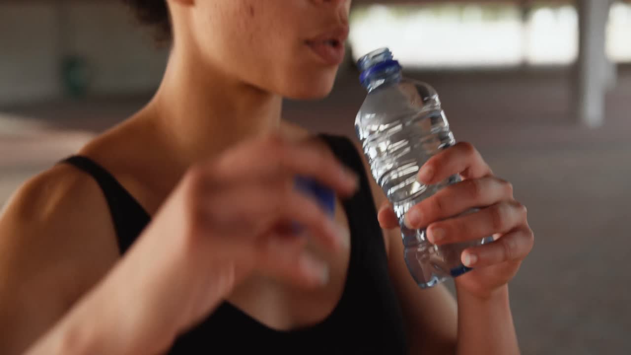 vista frontal de una joven mujer afroamericana bebiendo agua en la ciudad 4k