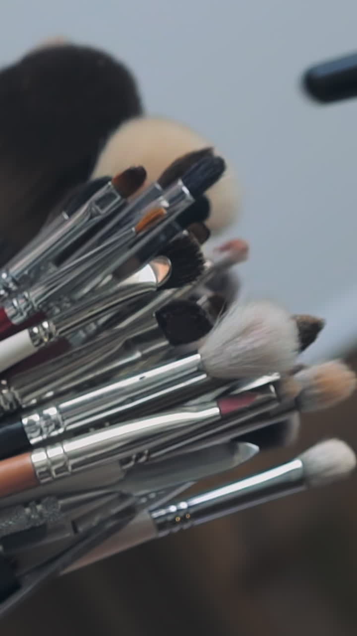 Makeup artist takes fluffy brush to work with client at table in contemporary beauty salon extreme closeup. Different tools and decorative cosmetics