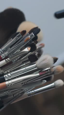 makeup artist takes fluffy brush to work with client at table in contemporary beauty salon extreme closeup. different tools and decorative cosmetics