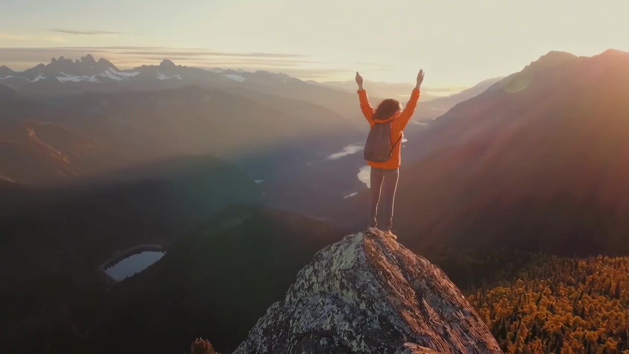 Donna escursionista con le braccia alzate su una cima di montagna al tramonto