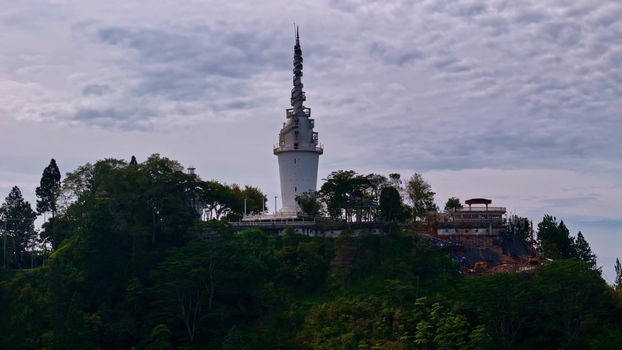 La Torre Ambuluwawa se eleva desde una cresta boscosa con edificios circundantes bajo un cielo nublado texturizado