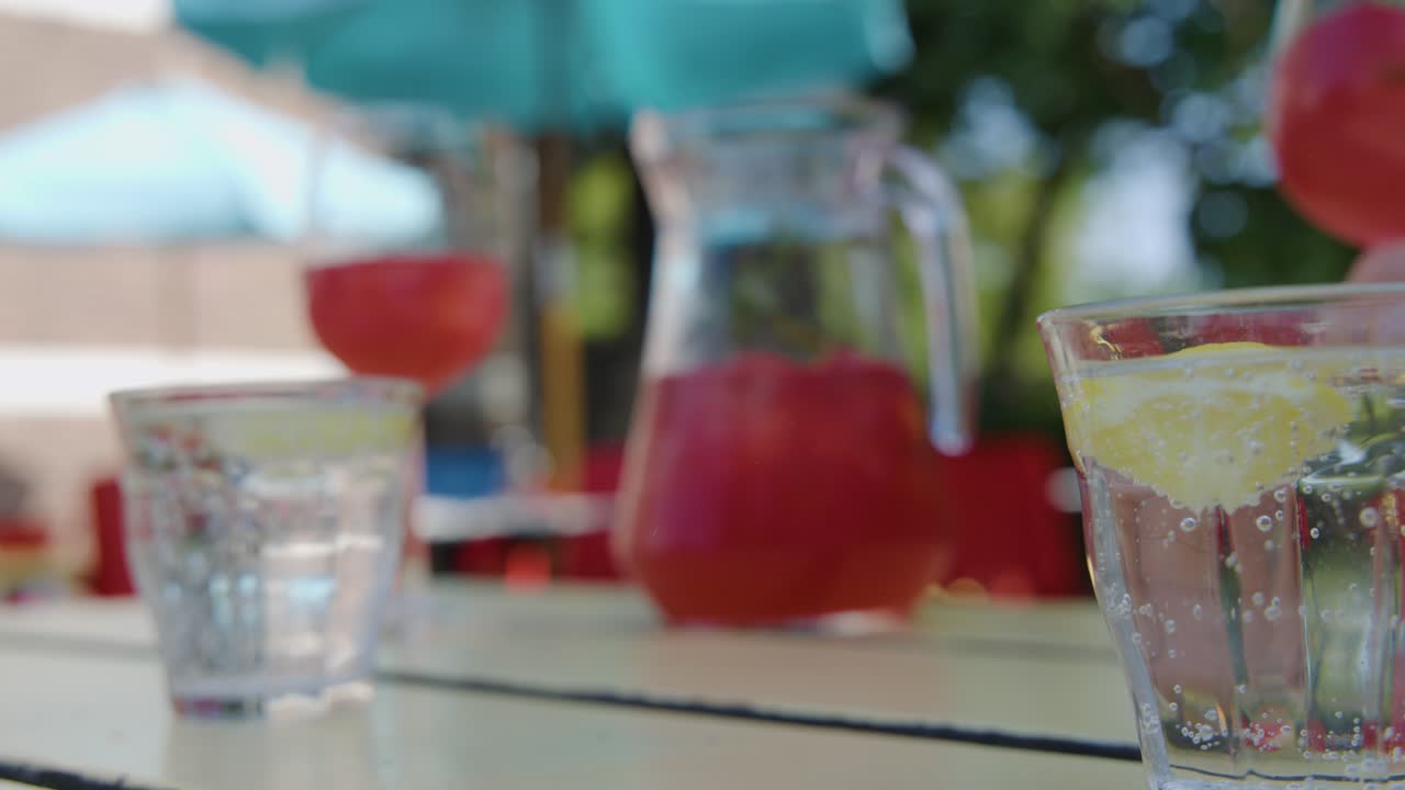 Hand pours red cocktail from wine glass into sparkling water with lemon, outdoor patio, daylight