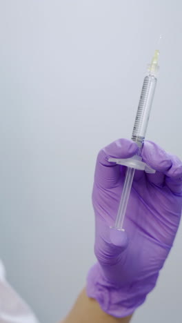 A beautician in purple gloves is holding an injection of a botulinum toxin in her hand at a medical cosmetology center. Close-up. Preparation to the procedure Vertical video