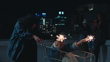 happy friends playing with shopping cart holding sparklers having fun on rooftop at night celebrating new years eve enjoying weekend party