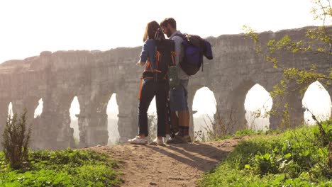 young lovely couple backpackers tourists reading map pointing directions roman aqueduct arches in parco degli acquedotti park ruins in rome on romantic misty sunrise with guitar and sleeping bag slow motion