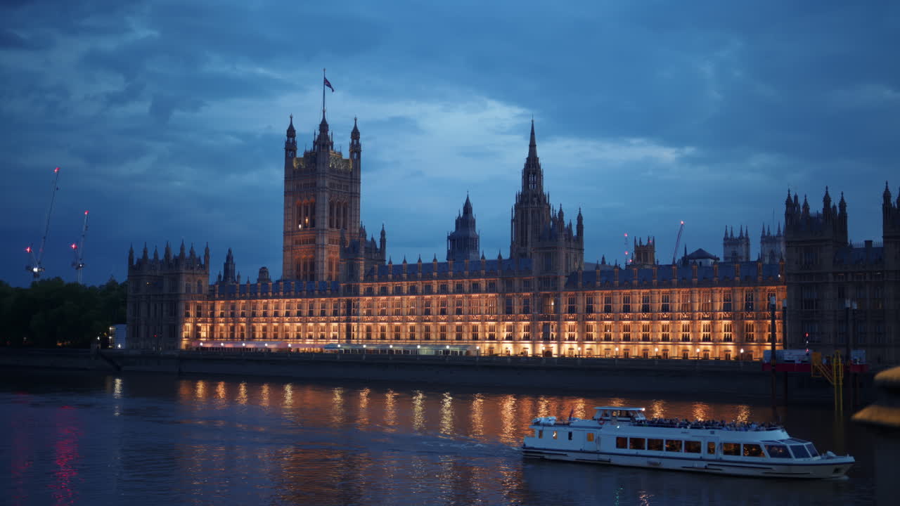 Utsikt over Palace of Westminster om natten med lysene reflektert i Themsen og en sightseeingbåt som passerer forbi, London, England