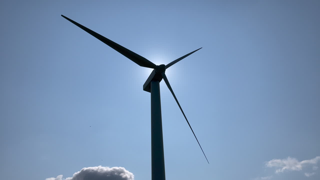 밝은 푸른 하늘을 배경으로 회전하는 풍력 터빈의 실루엣, 터빈 뒤에 있는 태양