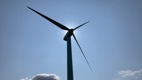 silhouette of a wind turbine spinning against a bright blue sky, sun behind the turbine