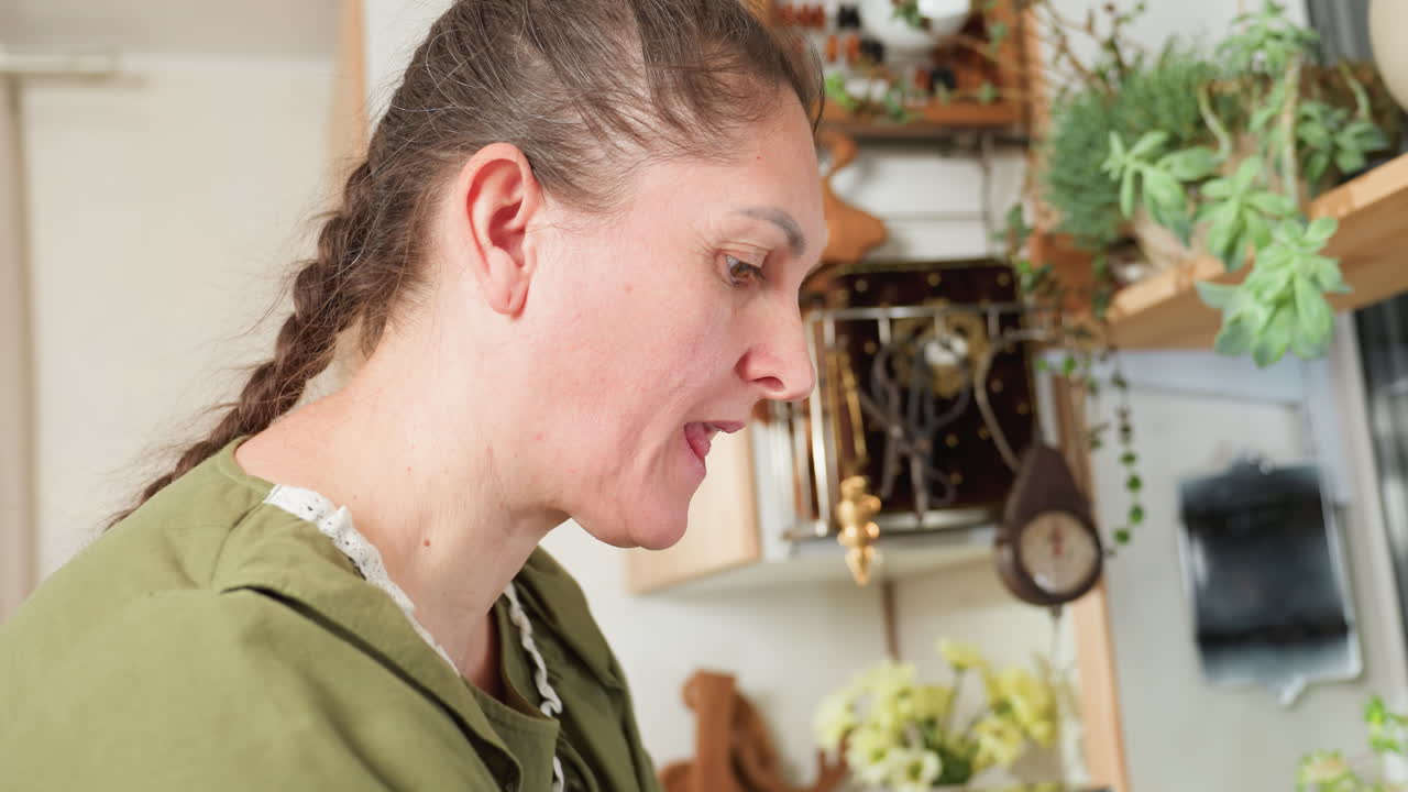 Housewife in green dress tastes food on fingertip while preparing something in cozy kitchen, deeply focused and enjoying cooking process, surrounded by plants and utensils