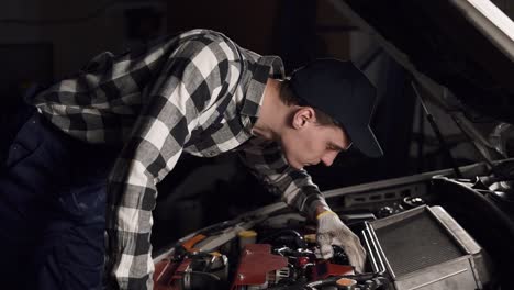 car service, repair, maintenance and people concept - mechanic man wearing work robe and cap working at workshop. inspecting all the mechanisms and their proper functioning.