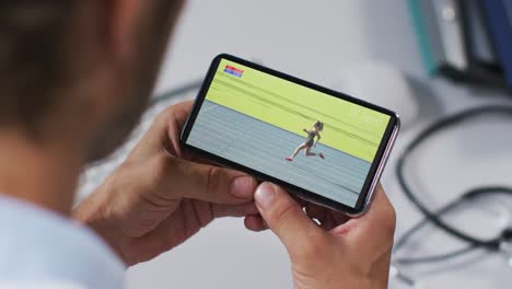 compuesto de un médico masculino viendo un evento de atletismo en un teléfono inteligente