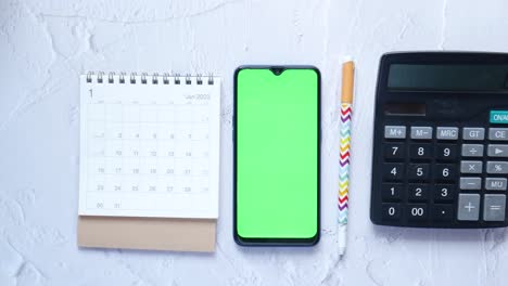 calendario abierto y teléfono inteligente con pantalla verde en la mesa,