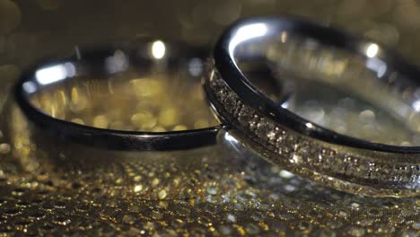 Wedding-rings-lying,-rotate,-spinning-on-shiny-golden-shining-surface-with-light,-close-up-macro