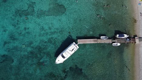 people swimming and relaxing on beach of budikovac blue lagoon with yacht and dinghy boats at jetty