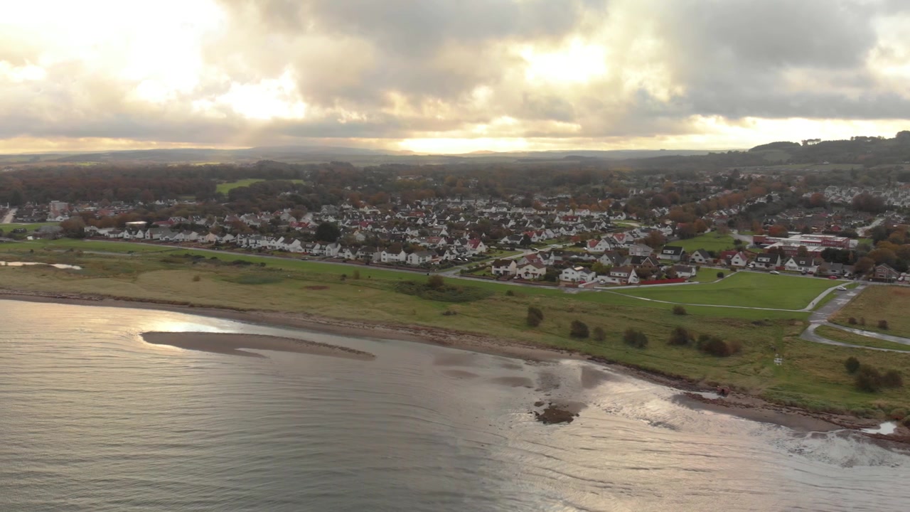 Aerial drone over Doonfoot, Ayr — beach, estuary and housing estate in autumn dusk light, Scotland.