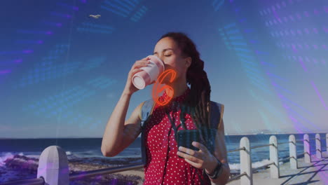 woman holding smartphone and coffee cup on seaside promenade, showcasing technology light overlays
