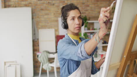 Video-of-biracial-female-artist-in-headphones-painting-in-studio