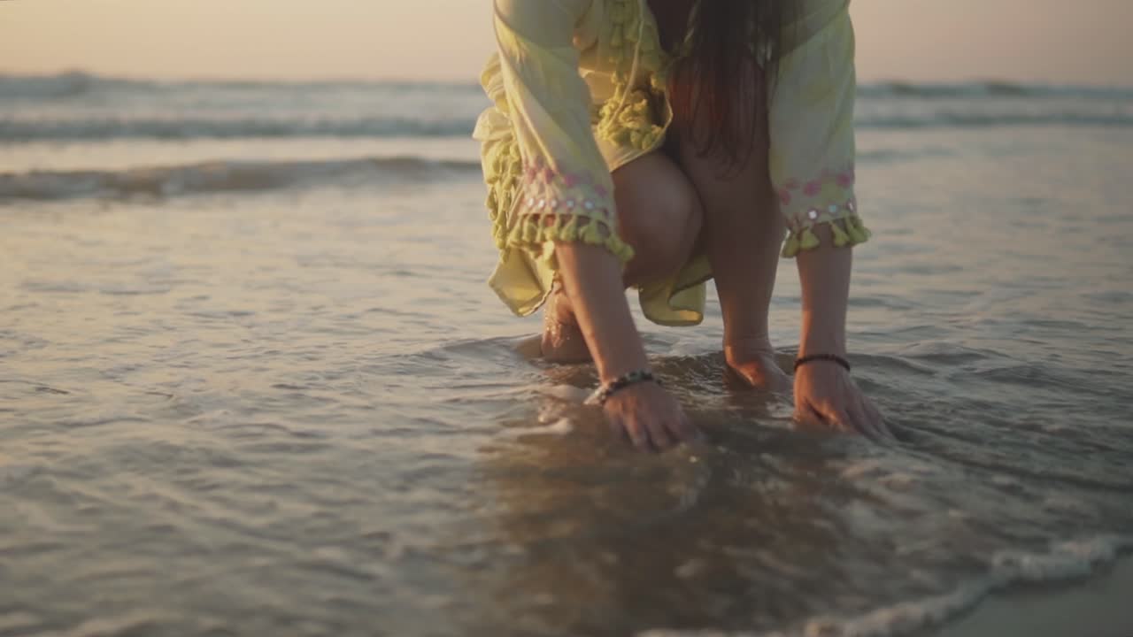 mujer en cuclillas en la orilla y jugando con agua mientras pequeñas olas espumosas lavan la arena