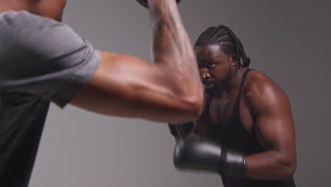 Studioaufnahme-Eines-Männlichen-Boxers-Beim-Sparring-Mit-Einem-Trainer,-Der-Schlagpolster-Oder-Handschuhe-Trägt-Und-Für-Den-Kampf-übt-3