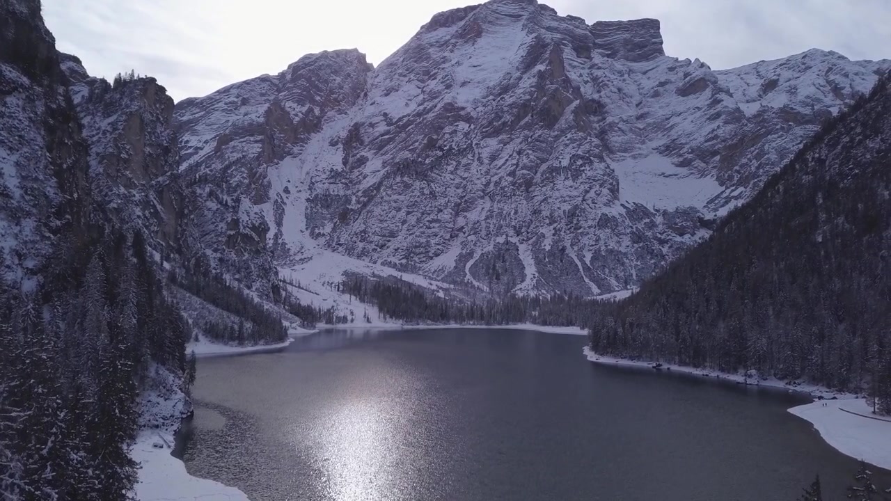 Un lago alpino immobile, il Lago di Braies, riflette cime innevate sotto un cielo invernale tenue, ideale per contenuti di viaggio o natura.