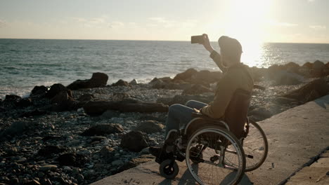 man in wheelchair taking selfie at sunset beach