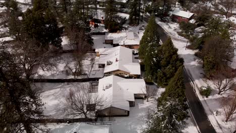 aerial shot of small rural town, rooftops covered in snow surrounded by pine trees in winter