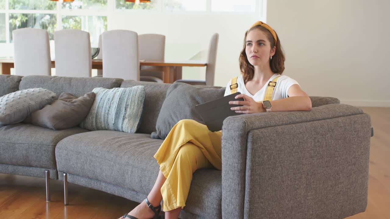 Donna che guarda contenuti su tablet mentre scorre, si ferma e guarda fuori dalla finestra sul divano, spazio per il testo