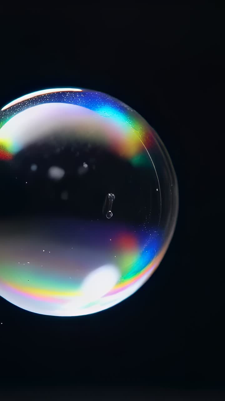 Video verticale: ago di metallo che fora una bolla di sapone in studio, rilasciando piccole goccioline brillanti