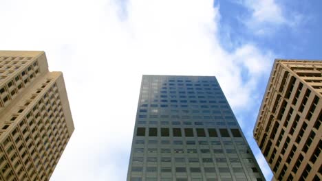 clouds and blue sky reflecting on windows of a building as they pass by