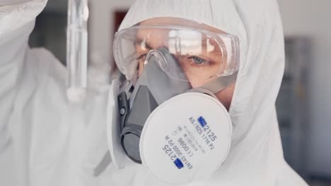 scientist in a protective suit and a respirator examining a substance in a test tube