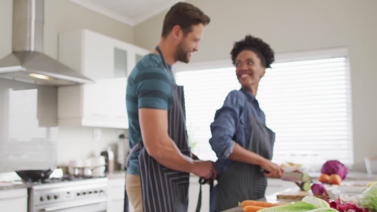 Video de pareja feliz y diversa preparando una comida, cortando verduras en la cocina