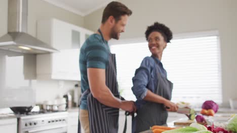 Video-of-happy-diverse-couple-preparing-meal,-cutting-vegetables-in-kitchen