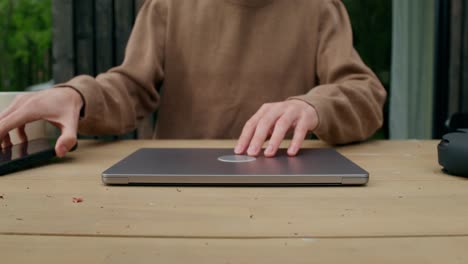 person working outdoors at a table with a laptop and phone