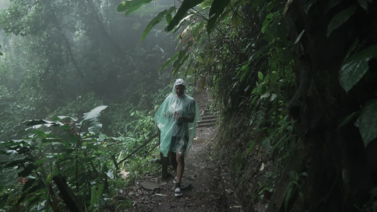 Man in poncho walks through rain forest in middle of rain storm, slow motion