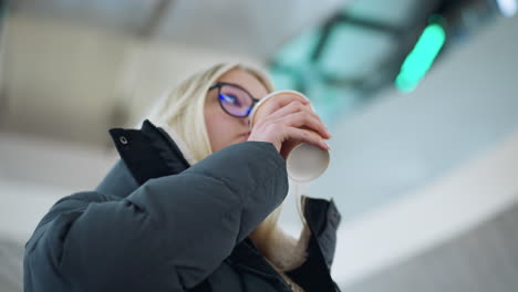 woman sipping beverage in black jacket inside a well-lit mall, captured closely, a moment of relaxation while enjoying a drink during a visit to a modern public space