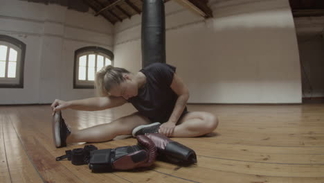 long shot of female kickboxer stretching legs on floor in gym