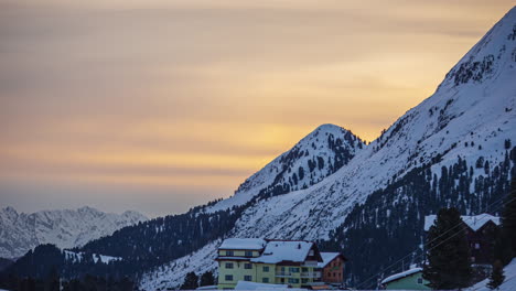 Orange-sky-with-clouds-moving-over-a-snowy-landscape-with-mountains-and-houses-and-people