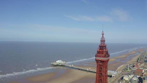 Aerial-footage,-drone-view-,-of-the-famous-Blackpool-Tower-and-beach-from-the-sky-on-a-beautiful-Summers-day-on-one-of-Great-Britains-most-popular-holiday-destinations,-tourist-attractions-by-the-sea