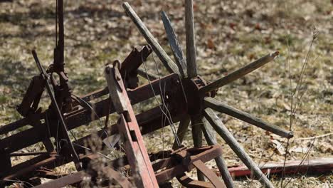 rundown old farm plow with wood wheels that have fallen apart sitting in the grass at a museum rusting away