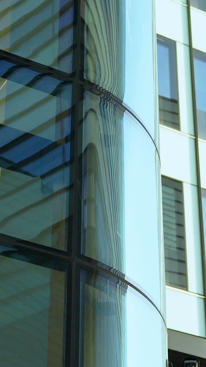 Una ripresa verticale di una facciata contemporanea di grattacielo in vetro con riflessi e una telecamera di sicurezza montata. Ideale per contenuti su affari, sicurezza e sviluppo urbano.
