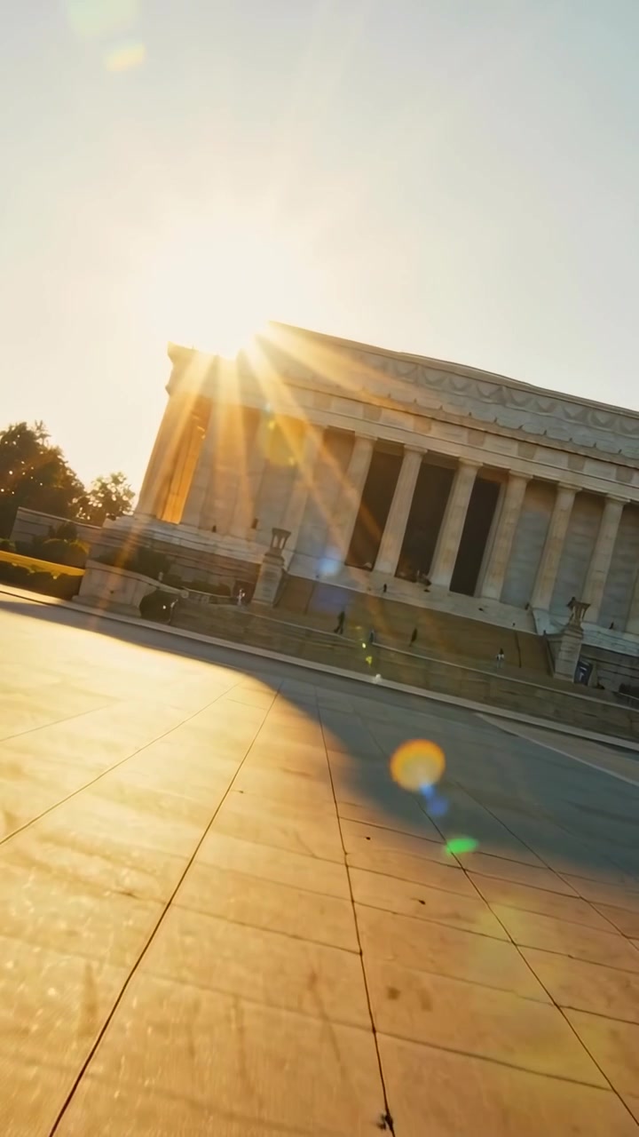Video verticale: Telecamera che segue un bagliore solare, filmando un monumento neoclassico in una piazza, con persone in movimento.