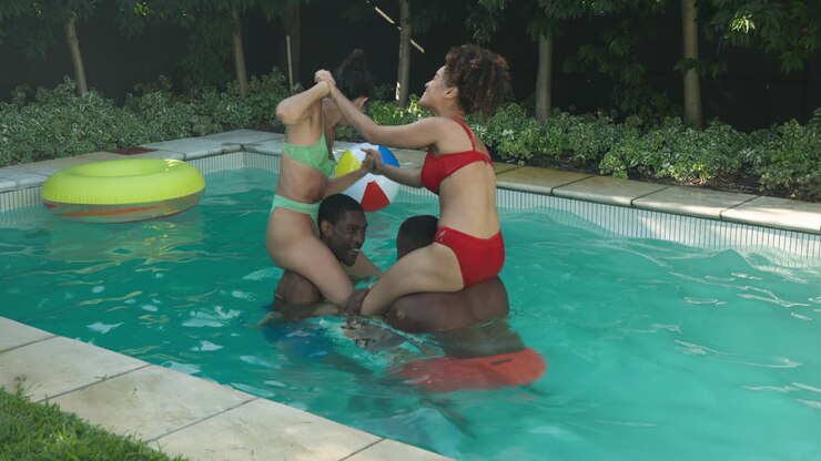 Diverse friends enjoying pool game, laughing and playing on inflatable rings in backyard