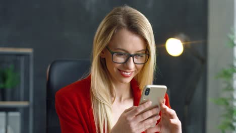 Blonde-Geschäftsfrau-Mit-Brille,-Die-Im-Büro-Ein-Smartphone-In-Den-Händen-Hält