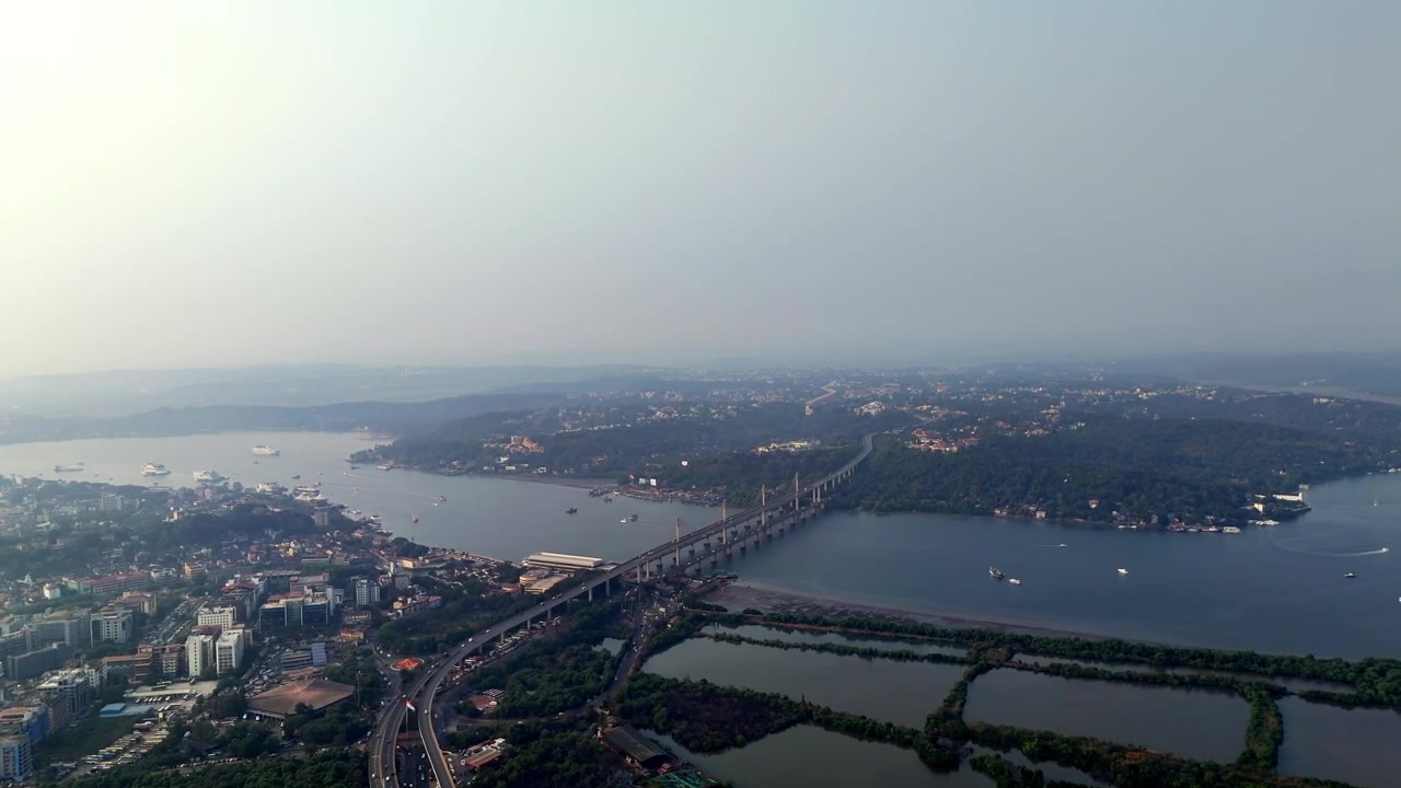 Veduta aerea cinematografica di una città costiera in inverno, dove un lungo ponte si estende su acque calme sotto un cielo morbido e velato, con insediamenti e isole distanti che sfumano nell'orizzonte nebbioso.