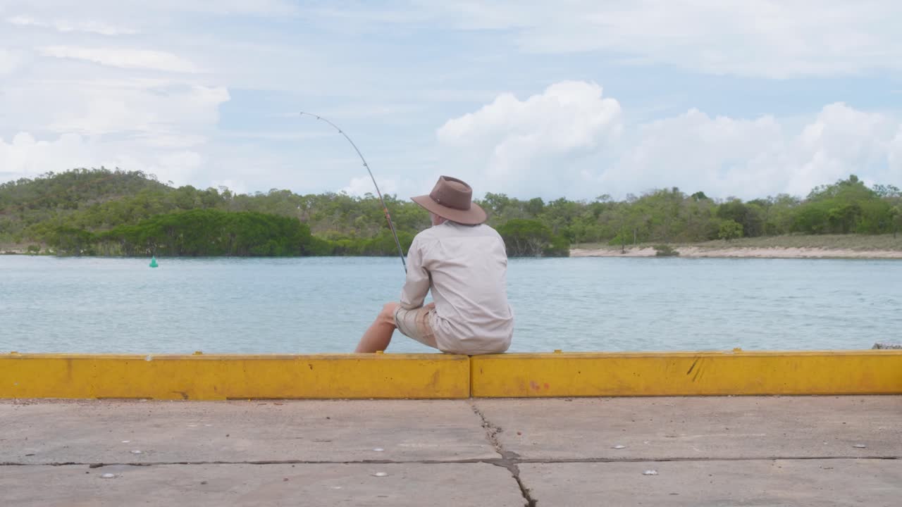 Man from outback Australia fishing from a remote pier on an overcast, wet season day. In slow motion, clip 5