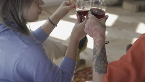 close up of two happy girls toasting with wine and sharing pizza at home