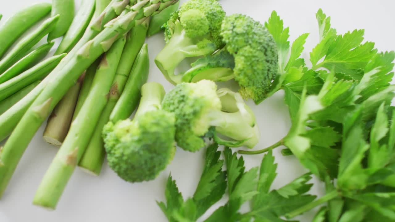 Video of close up of fresh green vegetables on white background