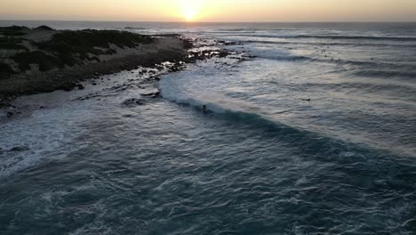 aerial following shot of surfer riding wave along coastline during golden hour in australia